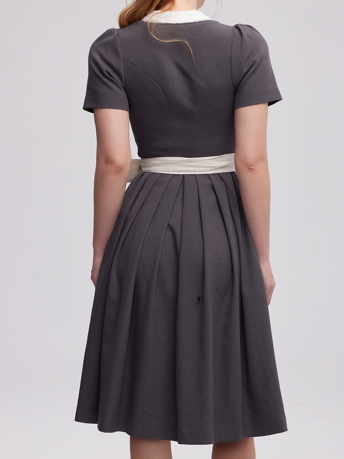 Ein graues Dirndl mit traditioneller Schürze und Spitzenbesatz
